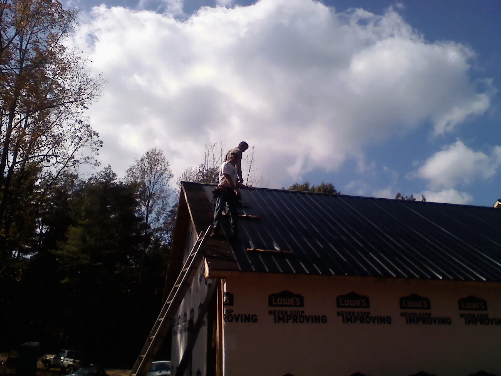 Roofer fastening dark metal panels high against a cloudy sky, from a Roof Inspection job in Ansonia